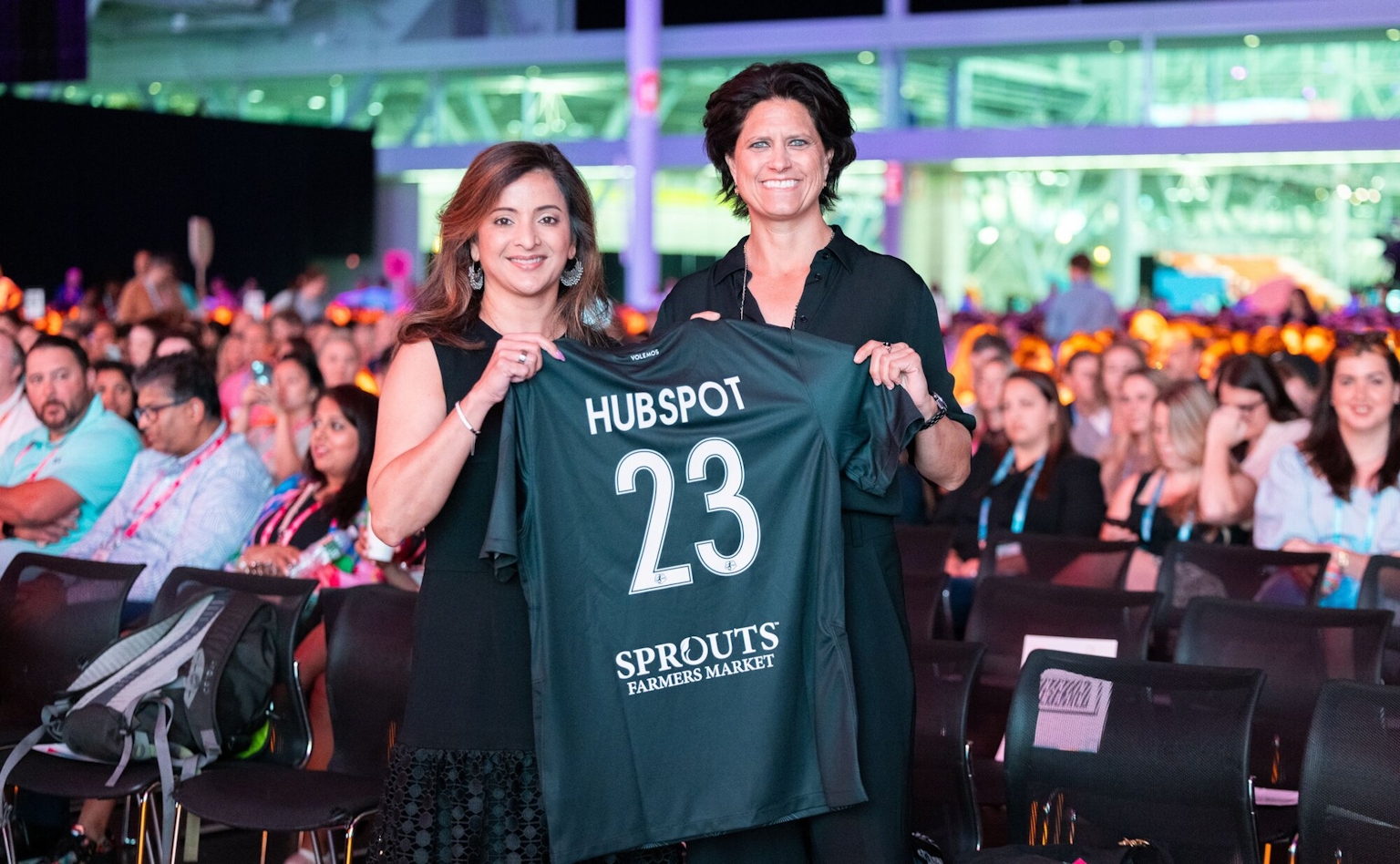 Two people presenting a sports jersey. It says "Hubspot" with the number 23."